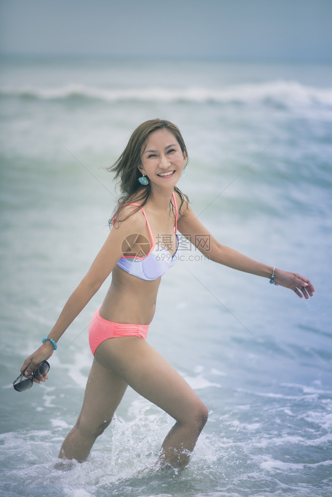 身着比基尼穿的美丽亚洲年轻女在海边滩面带笑脸放松女孩支撑图片