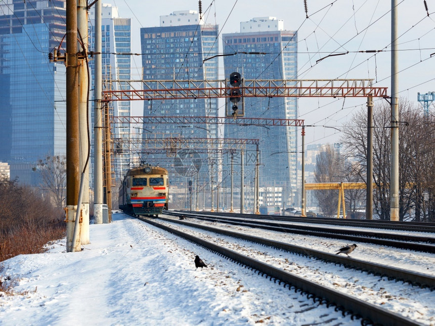 现代的上市一辆旧电动火车在冬季的轨道上行驶背景是城市观和在阳光下建造中的摩天大楼城市图片
