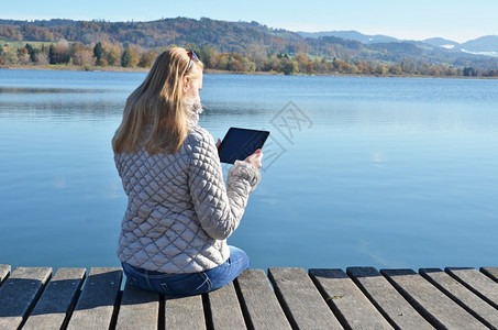 女孩在木制码头的石板上对着瑞士湖阅读书安静的互联网图片