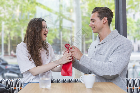 庆典约会吸引人的这是给你快乐男人给他爱妻送礼物女人满目欢喜地看着笑的情侣坐在餐厅桌前坐着背景图片