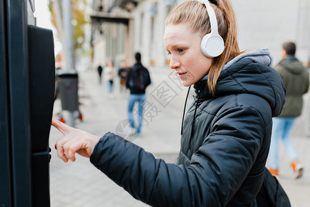 机器蓝色的年轻金发美女在城里付停车费脸上戴着耳机的夹克脸型惊讶的城市图片