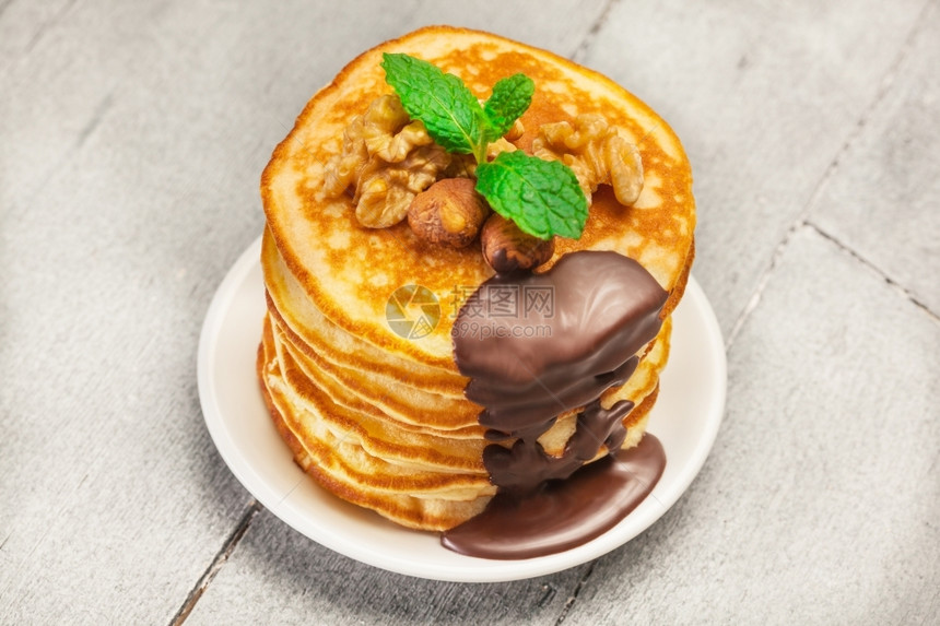 甜点绉盘子木制桌上加巧克力和坚果的煎饼照片图片