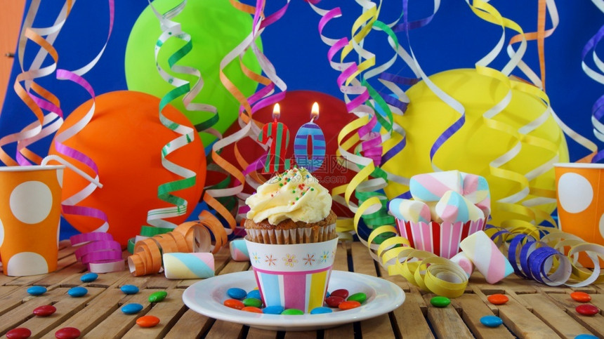 喜庆的火焰生日20小纸杯蛋糕在仿古木桌上燃烧着蜡烛背景是彩色气球塑料杯和糖果背景是蓝色派对墙背景甜点图片
