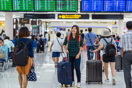 延迟朋友们手提箱携带行李的亚洲旅者在现代机场飞行信息屏幕登入旅行和带有技术概念的交通检查时看飞行机板上的载有李亚洲旅者亚洲人高清图片素材