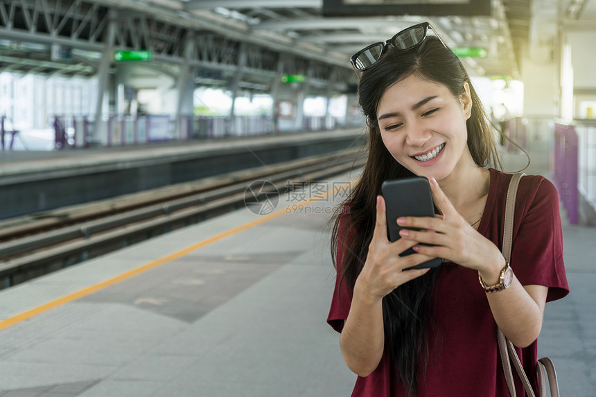 亚洲人利用BTSSkytrain铁路或MRT地的智能移动电话使用社交网络在大城市旅行生活方式和交通概念上搭乘临时穿便衣的亚洲女旅图片