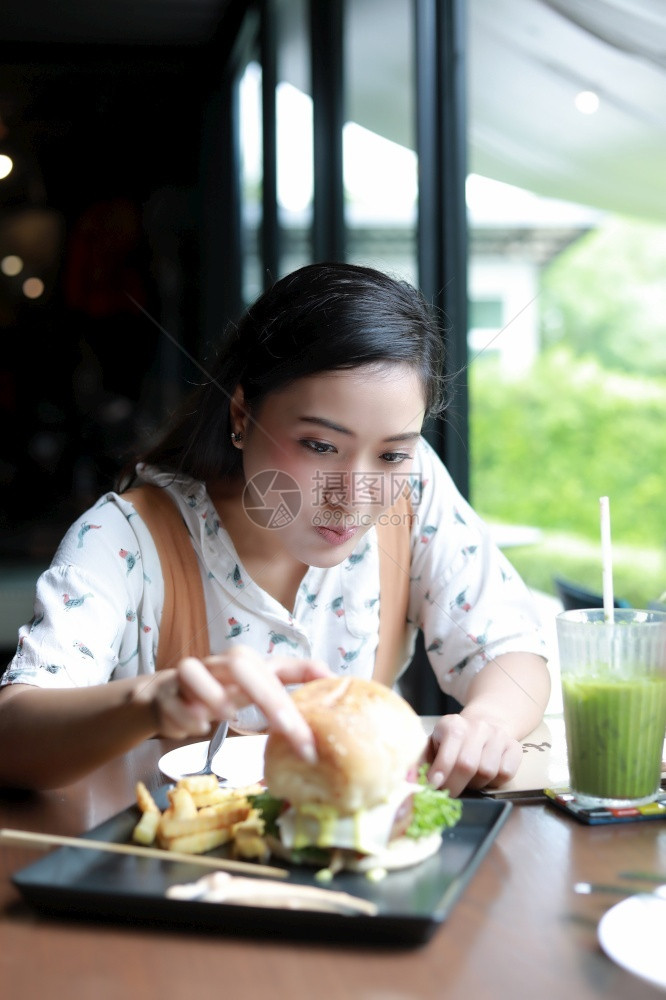 亚洲人漂亮的裔妇女微笑和快乐享受在咖啡和餐馆吃汉堡包的放松时间享受着请用图片