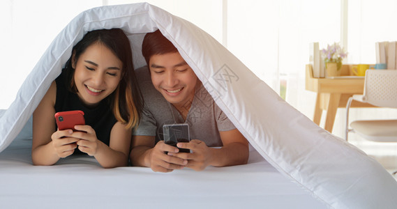 拥抱妻子亚洲情侣躺在床上玩手机躺在床的亚洲情侣海外图片