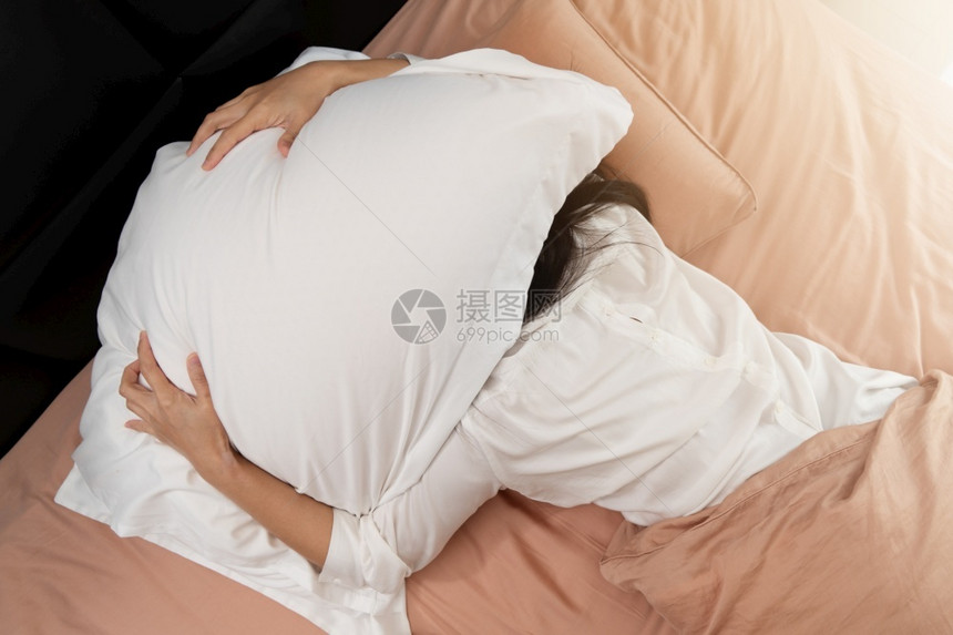 就寝时间钟睡不着的女人躲在枕头底下讨厌早上醒来的晨疲劳图片