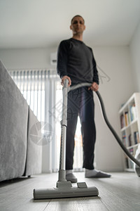 全长成年天主教男子使用吸尘清洁器洗家用木地板在白天前视线上做家务室卫生的男在家中用吸尘式真空器打扫房屋具地面子清洁图片