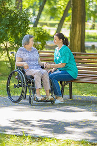 淑女残疾人在夏季公园户外轮椅运动室与残疾老年妇女交谈的护理员截瘫图片
