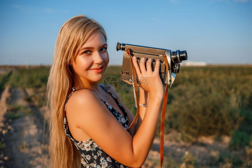 摄影师漂亮的魅力四射日落时在葡萄田中用古老的录像机拍摄着花粉印刷服装的金发女孩肖像图片
