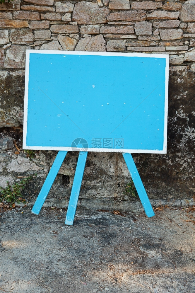 展示画架在一块旧石墙旁边的蓝色空白签牌复制文字空间外部图片
