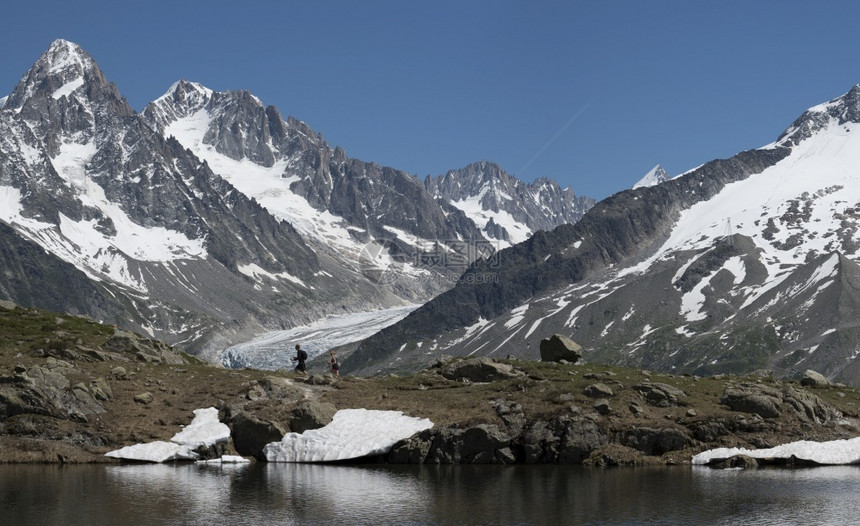 高的人们在山上一个湖边徒步旅行其背景是冰川和池塘小路图片