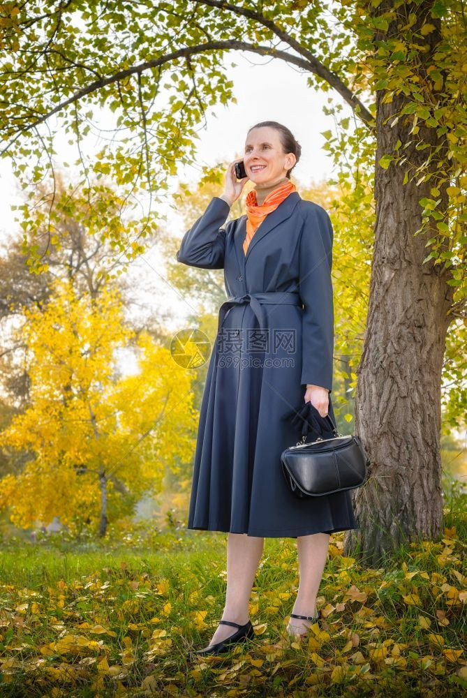 秋天在公园树下走来去的高级女商人手持移动电话袋和橙色围巾女士沟通图片