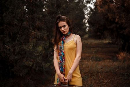 彩弹枪复古的常设一个年轻美丽的女孩肖像身着黄色洋装带彩围巾站在树林里拿着一个旧式手提箱丰富多彩的背景