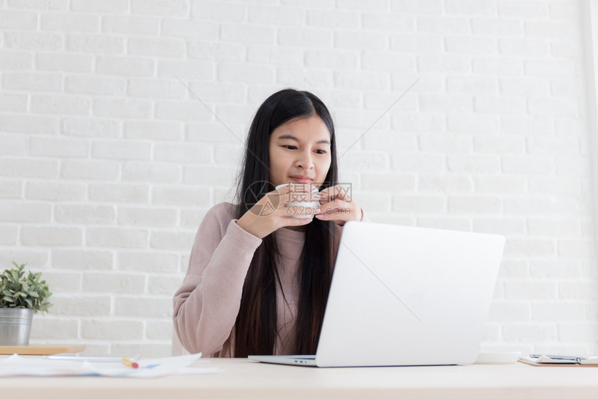 杯子肖像在职的拥有咖啡杯和办公室使用笔记本电脑的亚洲妇女新一代工作生活的概念20年图片
