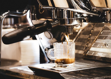 优质的滴香气浓缩咖啡机冲泡倒入店的玻璃杯中浓缩咖啡从机中倒出图片