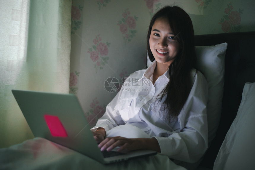 女士在职的亚裔妇女用笔记本在床上夜间工作她微笑并享受在家工作细胞图片