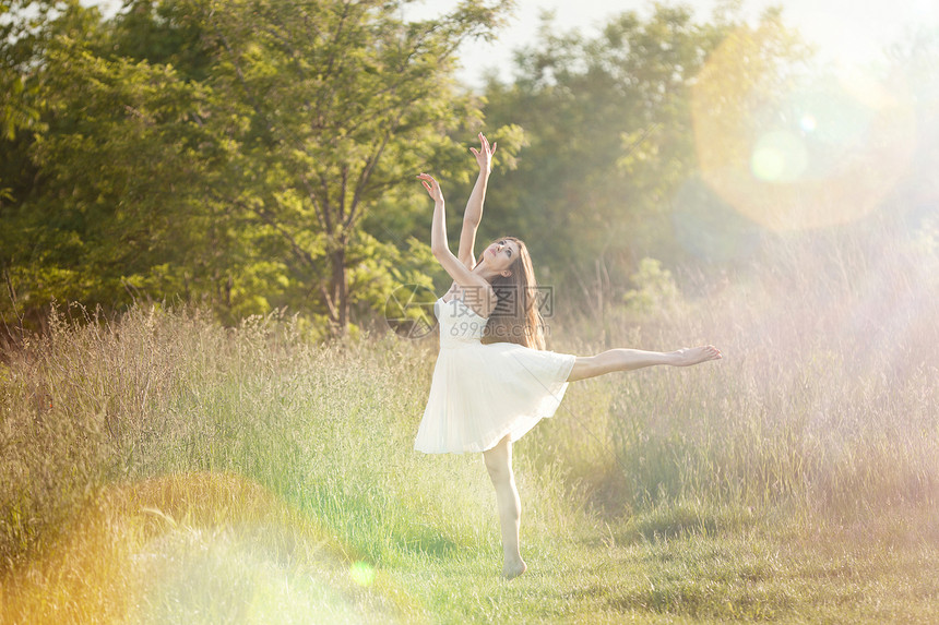 跳舞活动跃芭蕾者在草地上做阿拉伯礼仪穿着白裙子在自然背景和日落的光芒中图片