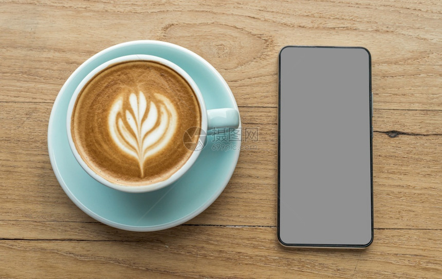 办公室食物黑色的带空灰屏幕的智能手机和带拿铁艺术牛奶泡沫的热咖啡拿铁杯在顶视图的木桌上作为早餐在咖啡厅的店在商务工作概念期间图片