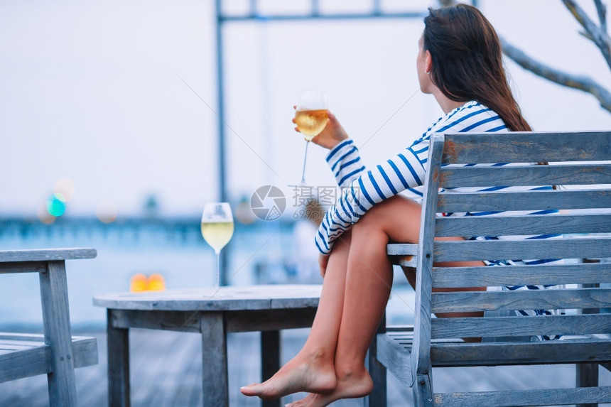 采取玻璃晚上在户外咖啡厅有白酒的年轻女孩在天堂岛暑假晚上在室外咖啡厅有白酒的年轻女孩产品图片