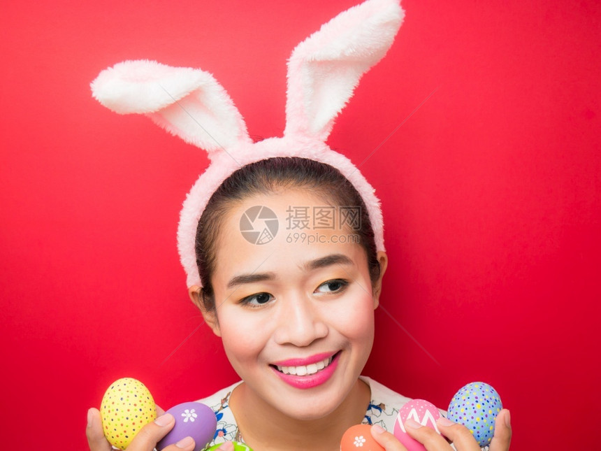 时髦的复活节戴兔子耳朵头带和携复活节鸡蛋的妇女有吸引力的年轻女微笑在明亮的红色背景上笑头巾运动型图片