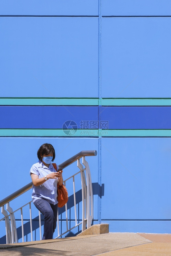 身戴保护面具的亚洲妇女在垂直架子上穿过多彩百花的货商店外面楼梯时使用智能手机随意的电话女士图片