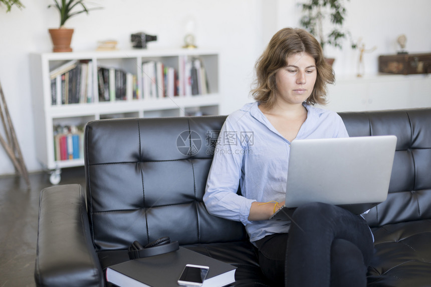 商业身着蓝衬衫的企业家妇女在沙发上用笔记本电脑工作联系青少年图片