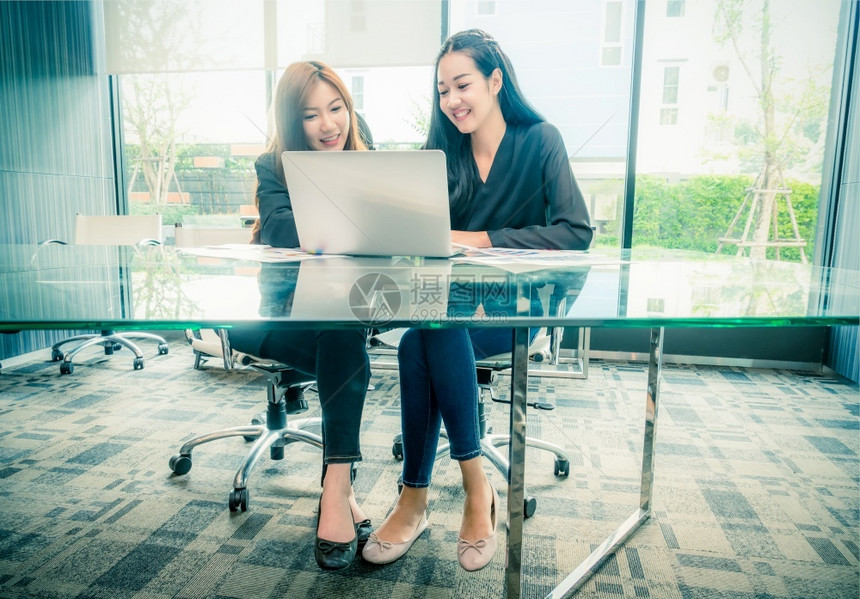 人白种在现代工作场所商业生活方式和技术概念中担任和使用技术笔记本电脑的两名亚洲青年女商务人座席并使用这些笔记本电脑女图片
