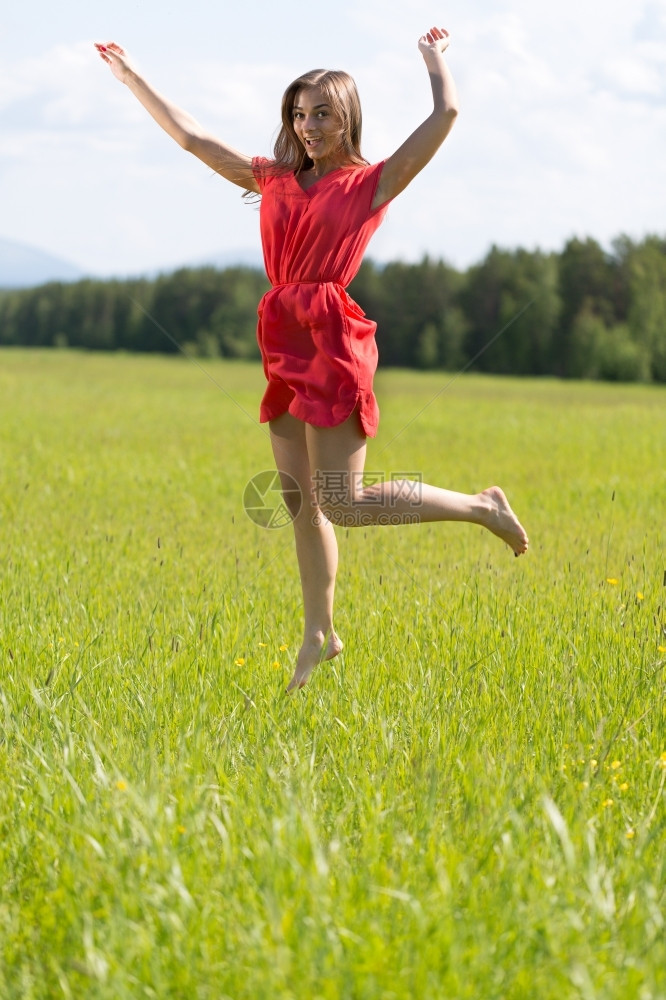 飞行自由穿红裙子的年轻女孩在阳光明媚的一天在田里跳跃种图片