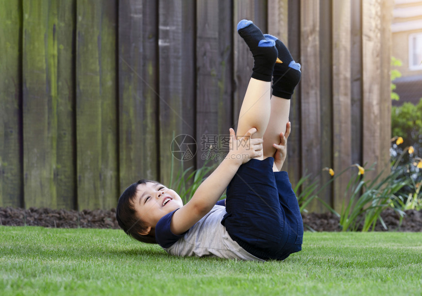 自然随意的白种人活跃孩子躺在花园草地上玩得开心健康男孩躺在草坪上抬起脚爬到天上去放松快乐的童年享受暑假概念快乐童年图片