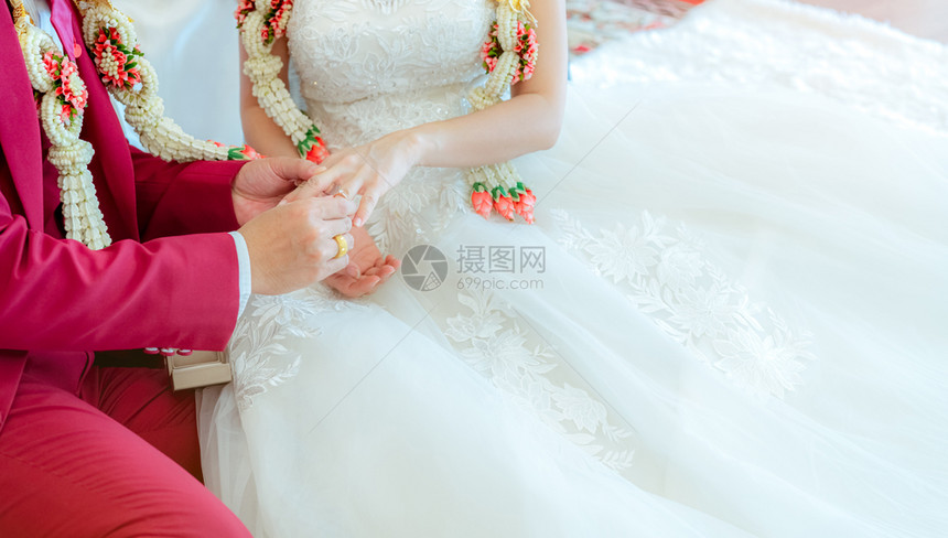 裙子妻Groom把结婚钻石戒指戴在新娘的手上以便在婚礼仪式当天提出求婚白礼服红西装和婚纱的新娘郎婚姻或后生活花朵图片