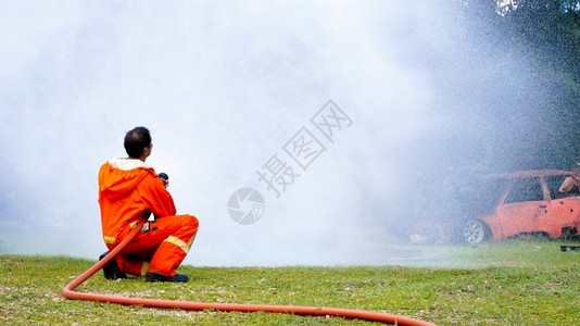 为了救援紧急情况消防员用水管化学泡沫喷洒剂发动机与火焰战斗的消防员Fierman戴硬帽身穿防火灭器方面的营救训练制服火花高清图片素材