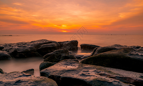 海滨日落时在石滩上的岩美丽海边夕阳天紫光海与空黄昏时的热带海风云天空和日落抽象背景平静放松生命景观港口黎明背景图片
