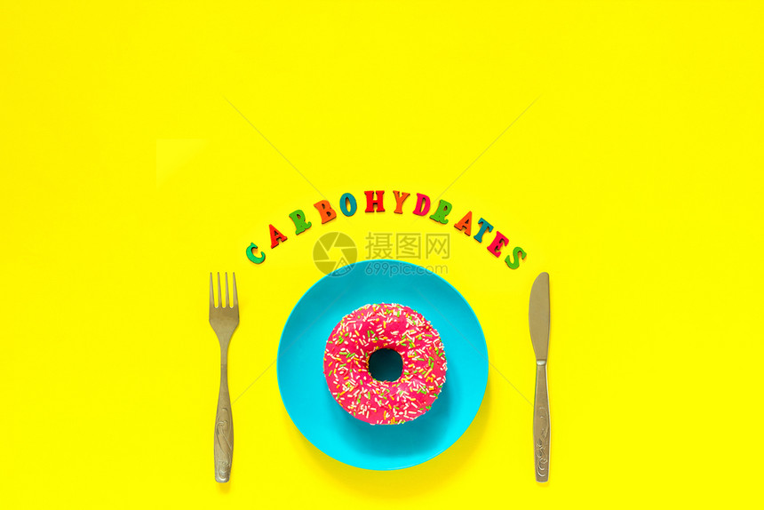面包店糖蓝色板上的粉红甜圈和餐具桌刀叉Text碳水化合物黄色背景的死活黄色背景的翻版空间上方视野平面观不满足日Carbo水合物蓝图片