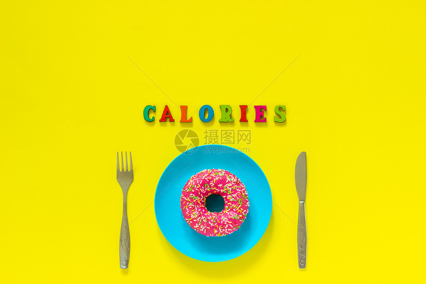蓝色板上的粉红甜圈和餐具桌刀叉上粉红色甜圈文本卡路里黄色背景的依然生命复制空间顶层视野平面观板胖的糖尿病育肥图片