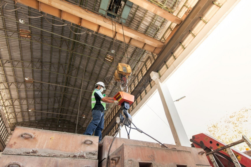 起重机一名亚洲男工程师身着保护设备的亚洲男工程师在厂中携带控制电缆吊索重铁钩抬起结构平台和大型钢箱的防护设备亚洲人金属图片