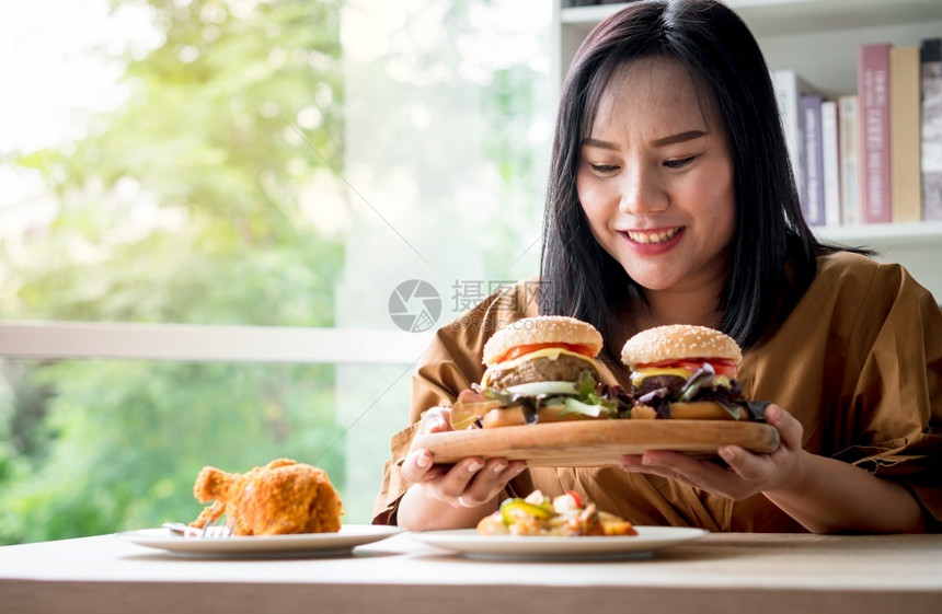 饥饿的超重女在分娩后将汉堡包放在木板上然后由送货员在家提供食物狂吃饮紊乱症BED概念与食用垃圾品放松成人蔬菜表示图片