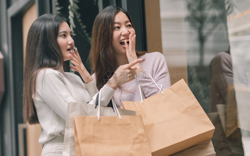 两个美丽的亚洲女令人惊讶持有纸袋和做窗户购物冬季节友谊和销售折扣概念笑声购买成人女士图片