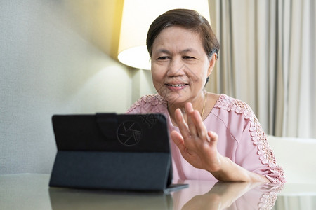 数字的喜笑亚洲老年妇女在隔绝期间数字平板电脑上播放视频话并在家里隔离快乐的老年女穿着粉红衣服手挥同时通过互联网技术与人们交谈国内泰国高清图片素材