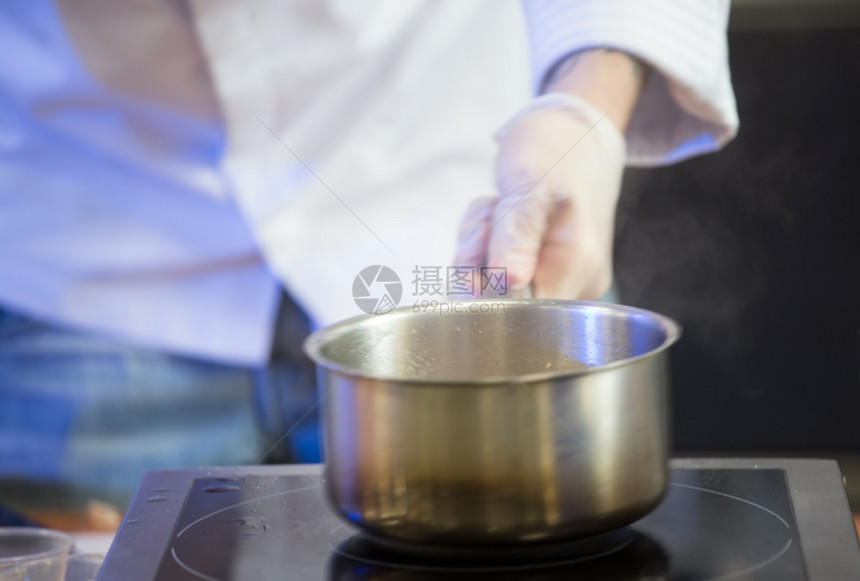 白手套上的Cookersqops手握着一个锅子在电炉上放个酱罐用有选择焦点白手套上的Cookrsqops双手在电炉上放个酱盆准备图片