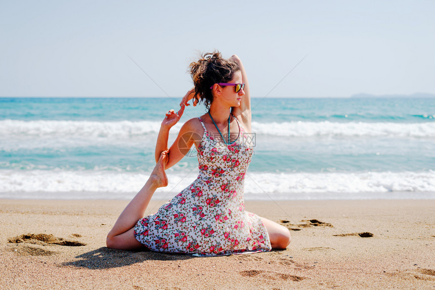海滨冷静的体式夏天穿着衣服的年轻女子在海边滩上练瑜伽在阳光明媚的白天在海边或图片