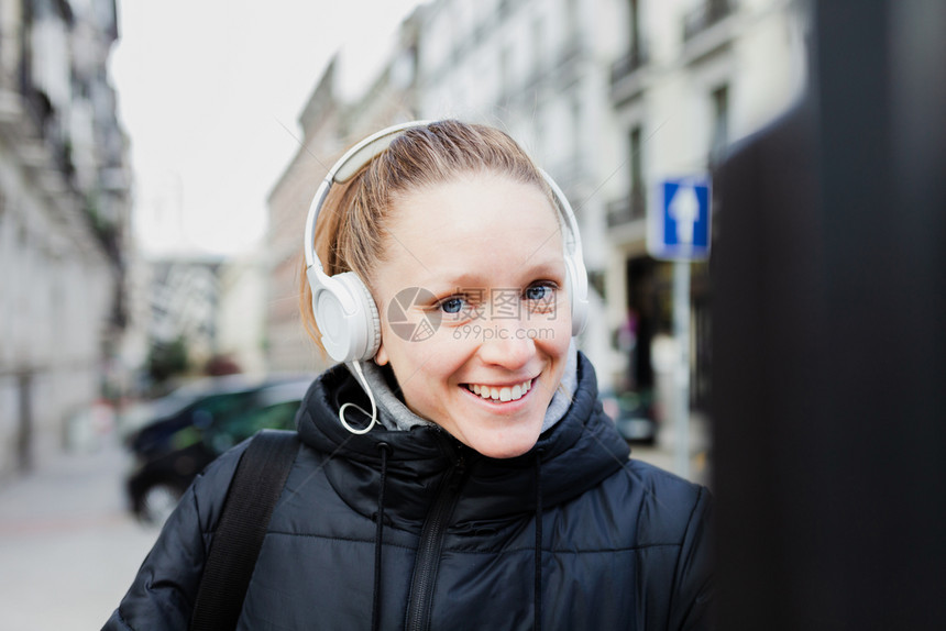 年轻金发美女在城里付停车费脸上戴着耳机的夹克脸型惊讶的女仪表快乐的图片