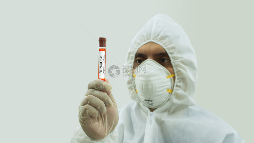 手套装戴面罩和生物防护服的医前视镜手持Covid19贴标签的血样测试管用手盯着白色底部的标称血样测试管并用手拿着标为Covid1图片