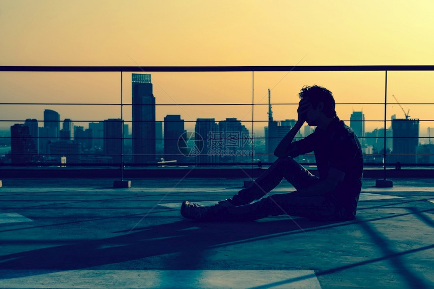 成人日落时坐在Bangkok城市风景的大楼屋顶上人头坐着一个压抑下来的男人看上去像休眠戏剧概念建造单身的图片