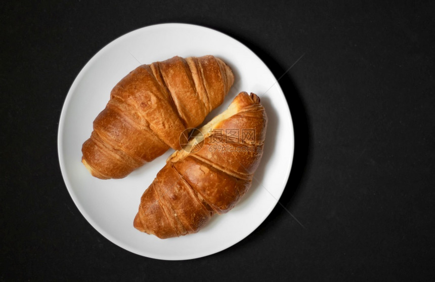 早餐金的子白色盘上新鲜烤面包的羊角在黑暗背景上一个白色盘子上图片