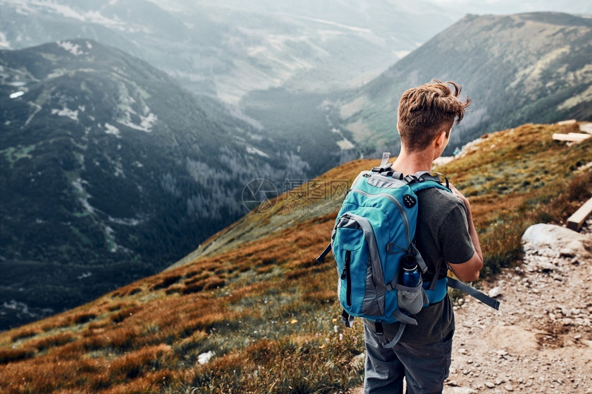 穆戈年轻人背着包在山里徒步旅行积极度过暑假少年从山顶沿着路走下来的后视图背包里徒步旅行的年轻人积极度过暑假漫游健康图片