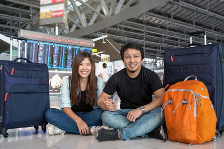 人们在现代机场旅行和运输概念的飞行信息屏幕登入飞行信息屏幕时坐在飞行板上着李和的亚洲夫妇旅行者在飞板上坐着白种人航班木板高清图片素材