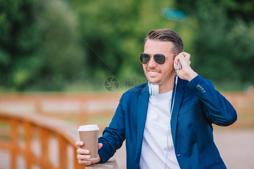 松弛成人男有智能手机的年轻人在户外喝咖啡快乐男孩在城市户外用手机工作欢乐城市青年男子在欧洲城户外工作喝咖啡和图片