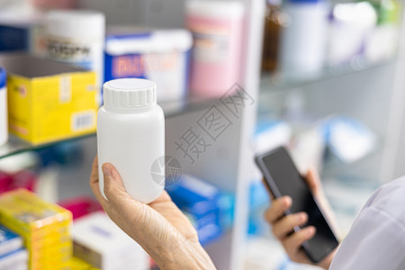 手持药剂师和品架底本的白瓶和智能手机子白色的店铺制服高清图片素材